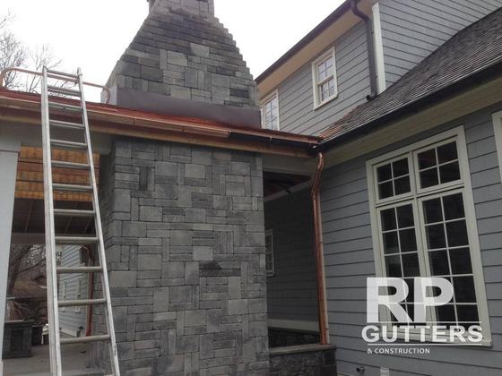 Copper gutters and downspouts on a stone and shingle home