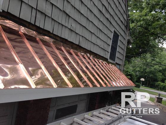 Copper roof edge along a shingled wall