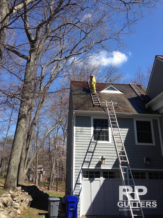 Roofer on a ladder at a gray shingled home